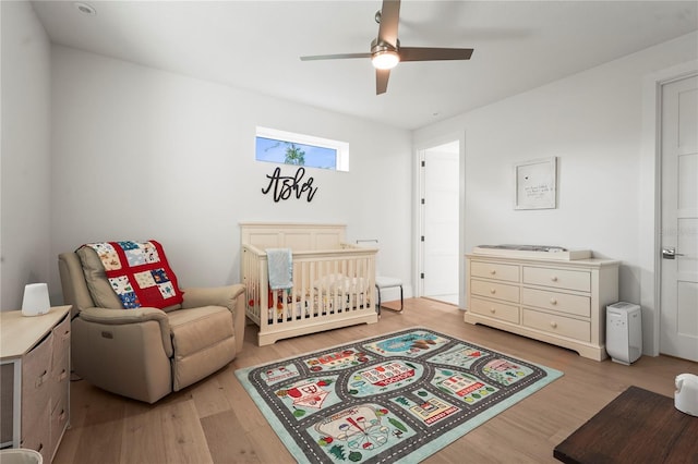 bedroom featuring a nursery area, wood finished floors, and a ceiling fan