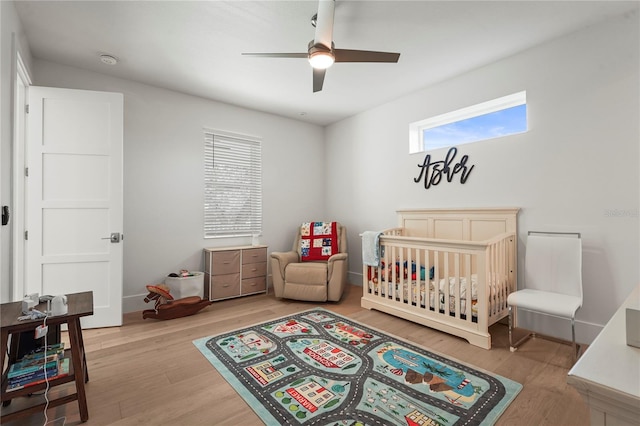 bedroom with ceiling fan, a nursery area, and wood finished floors