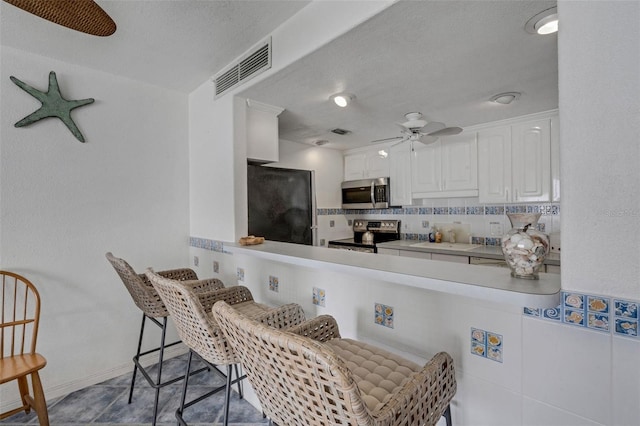 kitchen with appliances with stainless steel finishes, ceiling fan, kitchen peninsula, white cabinets, and tasteful backsplash