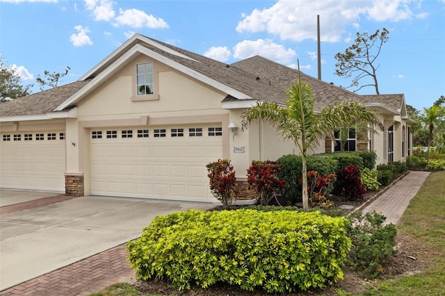 view of front facade featuring a shingled roof, concrete driveway, an attached garage, and stucco siding