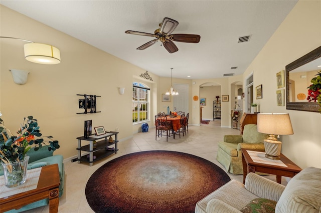 living room featuring arched walkways, light tile patterned floors, ceiling fan with notable chandelier, visible vents, and baseboards