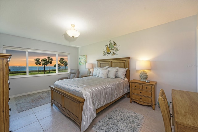 bedroom featuring a water view, light tile patterned floors, and baseboards