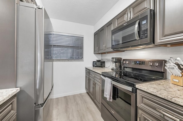 kitchen featuring baseboards, light wood finished floors, appliances with stainless steel finishes, light stone countertops, and tasteful backsplash