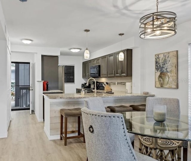 kitchen featuring dark brown cabinetry, a peninsula, light wood-style floors, a kitchen bar, and black microwave