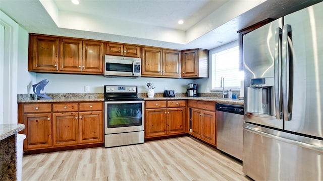 kitchen featuring light hardwood / wood-style flooring, sink, stainless steel appliances, a raised ceiling, and light stone countertops