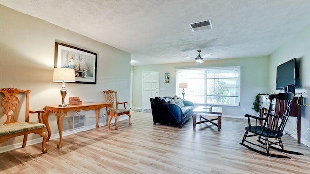 living area with a textured ceiling, ceiling fan, and light hardwood / wood-style floors