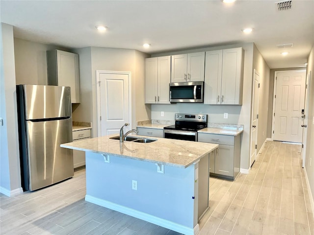 kitchen with a center island with sink, a kitchen breakfast bar, stainless steel appliances, light stone counters, and sink