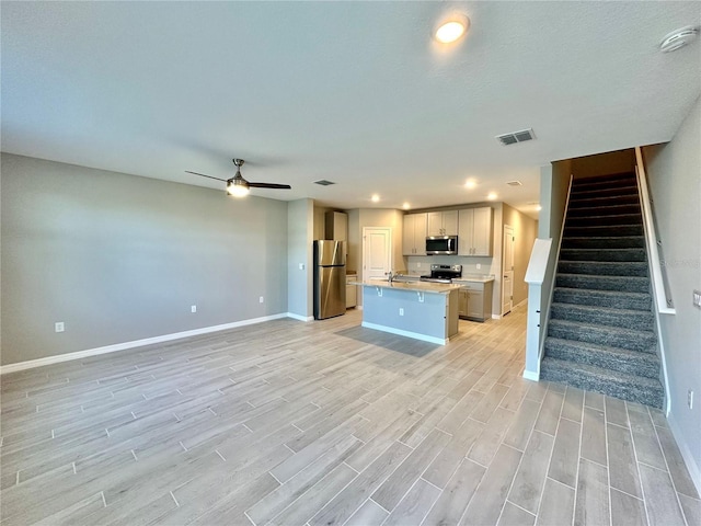 kitchen with stainless steel appliances, a center island, light hardwood / wood-style flooring, ceiling fan, and a kitchen bar