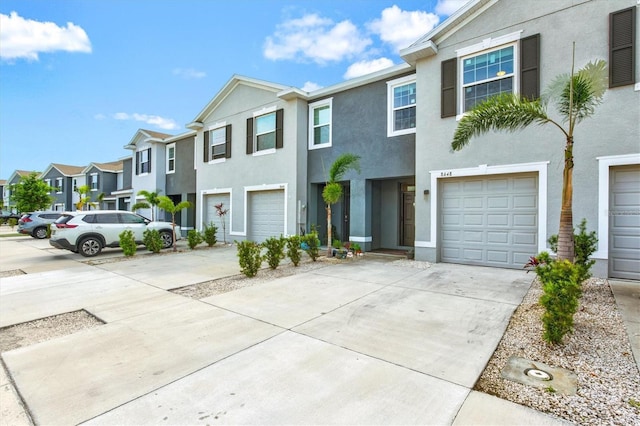 townhome / multi-family property featuring driveway, an attached garage, a residential view, and stucco siding