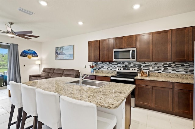 kitchen with open floor plan, decorative backsplash, stainless steel appliances, a ceiling fan, and a sink