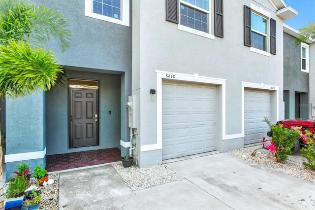 property entrance with stucco siding, driveway, and an attached garage