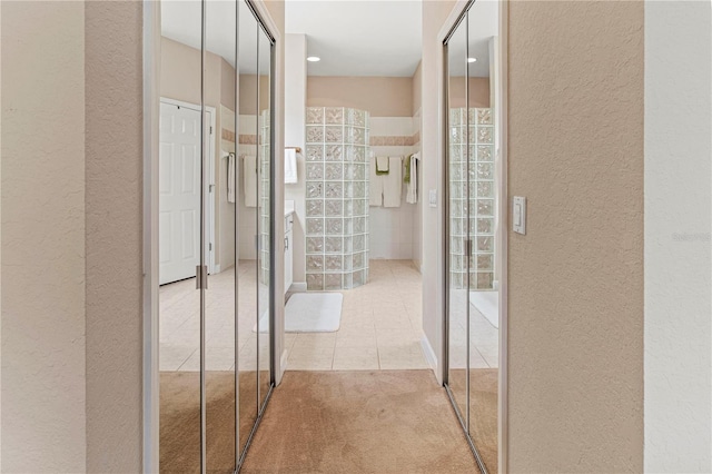 hallway featuring light carpet, light tile patterned floors, and a textured wall