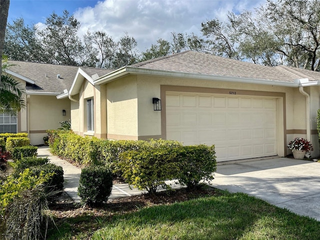 view of side of property with a garage, roof with shingles, concrete driveway, and stucco siding