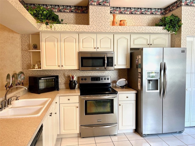 kitchen featuring light tile patterned floors, stainless steel appliances, light countertops, a sink, and wallpapered walls