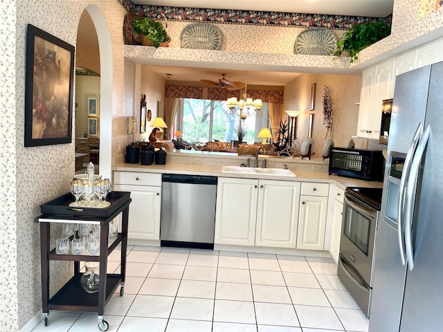 kitchen with wallpapered walls, stainless steel appliances, light countertops, white cabinetry, and a sink