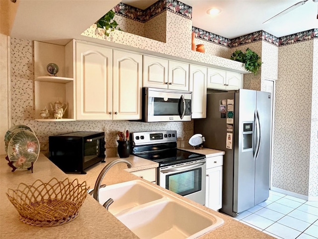 kitchen featuring wallpapered walls, stainless steel appliances, light countertops, a sink, and light tile patterned flooring