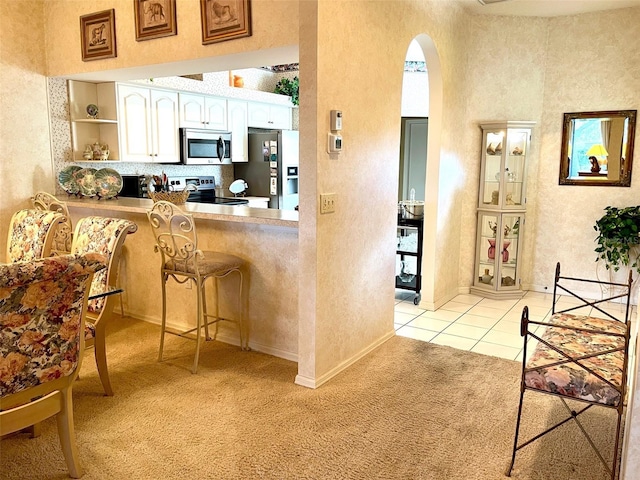 kitchen featuring arched walkways, a breakfast bar, appliances with stainless steel finishes, white cabinetry, and light carpet