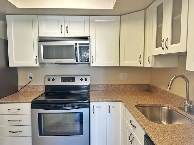 kitchen with stainless steel appliances, white cabinetry, a sink, and light stone counters