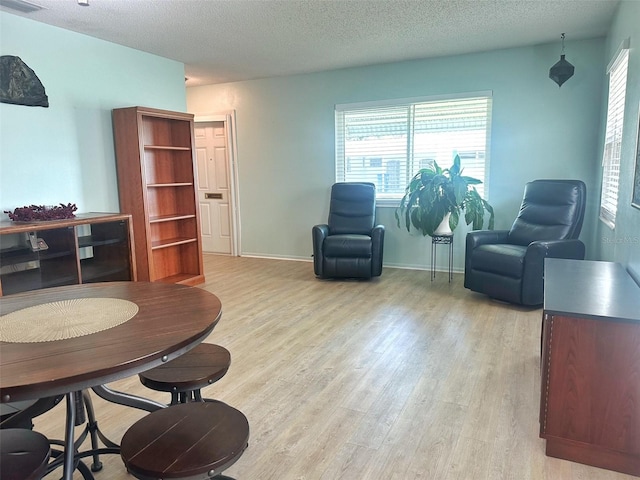 living area featuring baseboards, visible vents, light wood-style flooring, and a textured ceiling