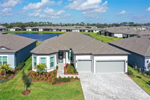 single story home with a garage, a shingled roof, a residential view, a water view, and decorative driveway