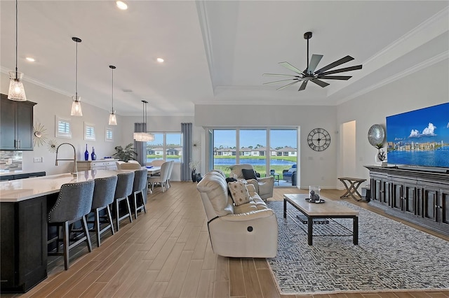 living room featuring light wood finished floors, a raised ceiling, a ceiling fan, ornamental molding, and recessed lighting