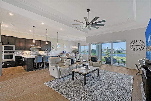 living area featuring ceiling fan, recessed lighting, ornamental molding, light wood-type flooring, and a raised ceiling