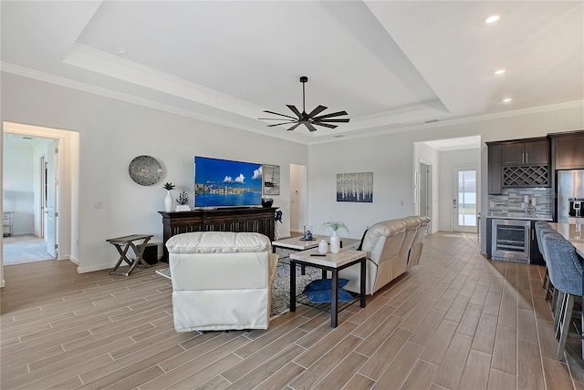 living area with beverage cooler, wood finish floors, a raised ceiling, and crown molding