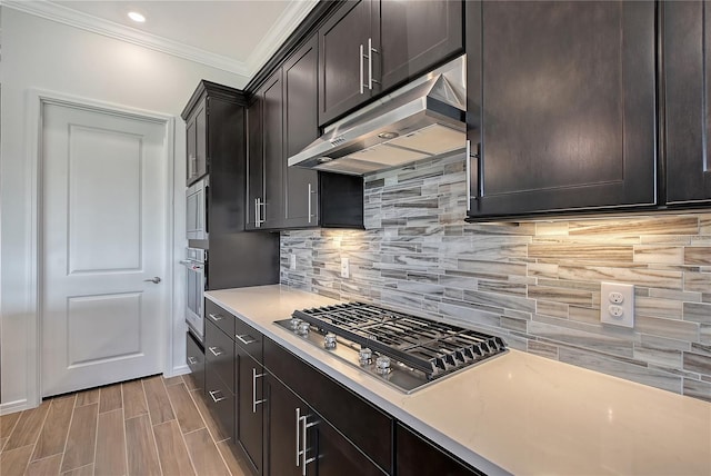 kitchen with dark brown cabinetry, under cabinet range hood, stainless steel appliances, light countertops, and tasteful backsplash