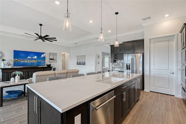 kitchen with wood finish floors, light countertops, hanging light fixtures, appliances with stainless steel finishes, and a kitchen island with sink