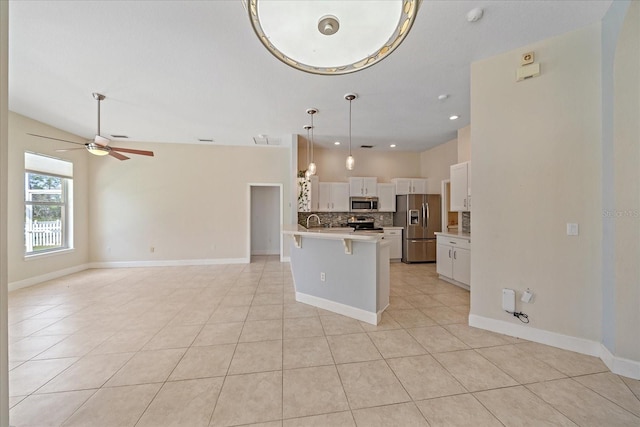 kitchen with appliances with stainless steel finishes, hanging light fixtures, an island with sink, white cabinetry, and a kitchen bar