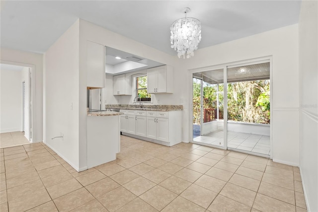 kitchen with light tile patterned floors, an inviting chandelier, white cabinets, a sink, and light stone countertops