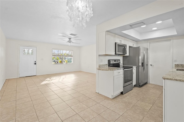 kitchen with stainless steel appliances, a raised ceiling, visible vents, white cabinets, and ceiling fan with notable chandelier