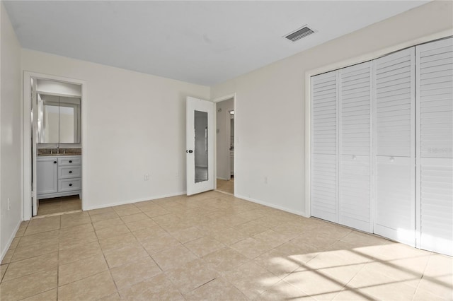 unfurnished bedroom featuring ensuite bathroom, light tile patterned flooring, visible vents, baseboards, and a closet