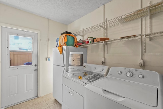 laundry area with laundry area, washer and clothes dryer, a textured ceiling, and light tile patterned floors