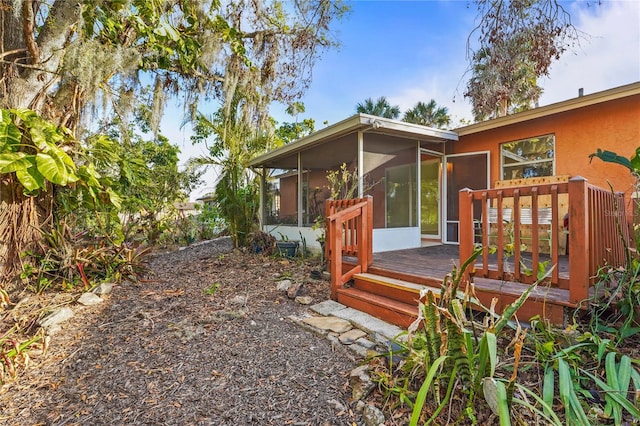 exterior space with a sunroom, a wooden deck, and stucco siding