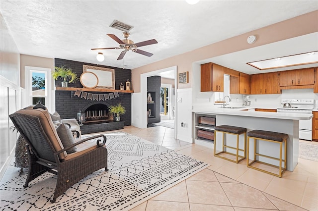 living area featuring light tile patterned floors, a textured ceiling, visible vents, a ceiling fan, and a brick fireplace