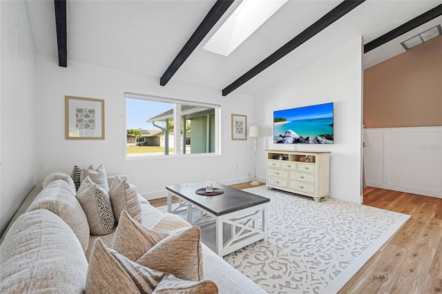 living area with lofted ceiling with skylight, wood finished floors, and wainscoting