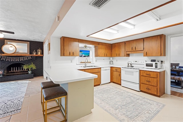 kitchen with white appliances, light tile patterned floors, brown cabinetry, ceiling fan, and a sink