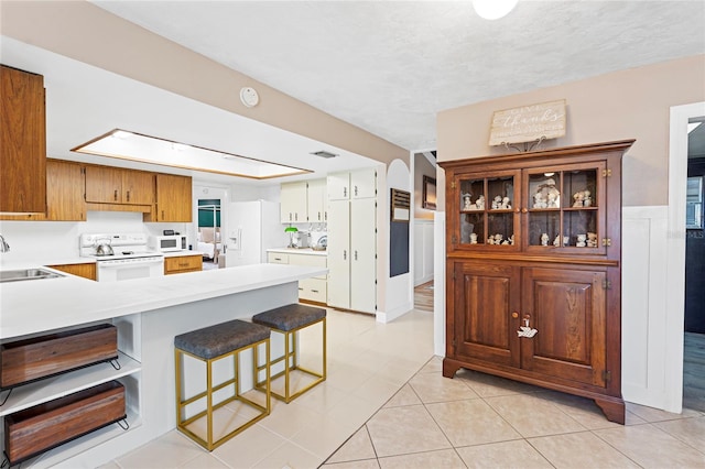 kitchen with arched walkways, a peninsula, white appliances, a sink, and light countertops