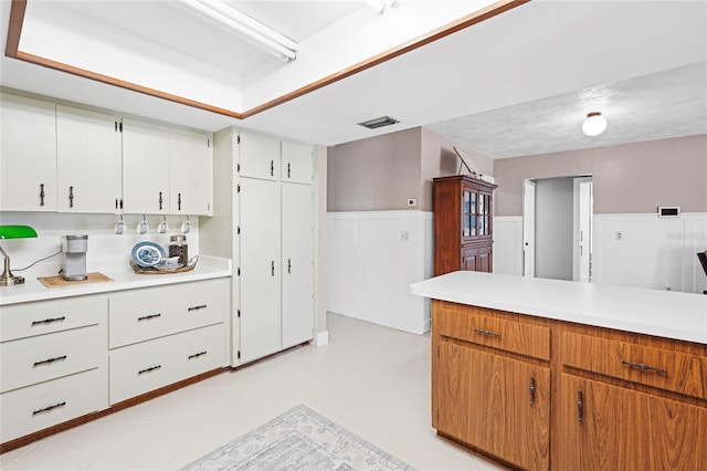 kitchen featuring light tile patterned flooring, visible vents, white cabinets, light countertops, and wainscoting