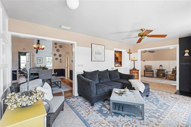 tiled living room featuring a textured ceiling and ceiling fan with notable chandelier