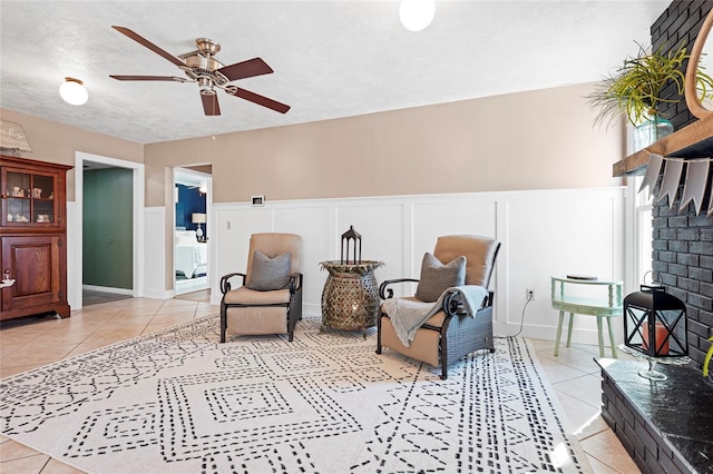 living area featuring a wainscoted wall, a ceiling fan, a textured ceiling, and light tile patterned flooring