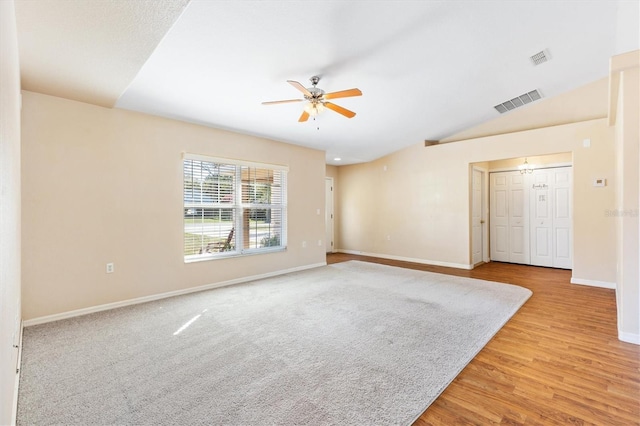 empty room with visible vents, vaulted ceiling, ceiling fan, light wood-type flooring, and baseboards