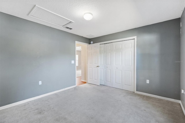 unfurnished bedroom with light carpet, a closet, attic access, and baseboards