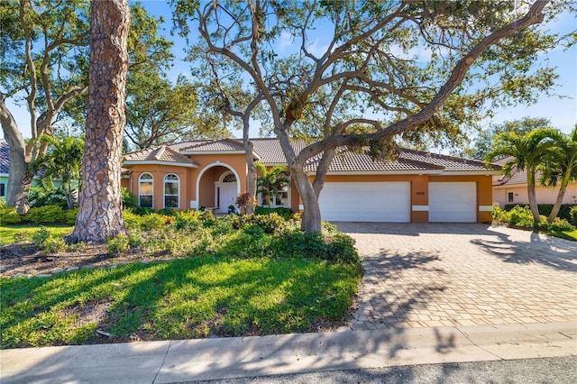 mediterranean / spanish home featuring a tile roof, decorative driveway, an attached garage, and stucco siding