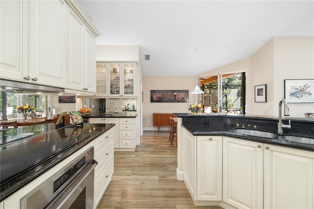 kitchen featuring glass insert cabinets, stainless steel oven, light wood-style floors, hanging light fixtures, and a sink