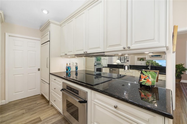 kitchen featuring stainless steel oven, light wood-style flooring, dark stone countertops, and white cabinetry