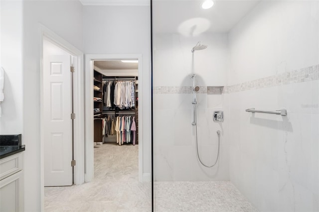 full bath featuring vanity, tiled shower, a walk in closet, and ornamental molding