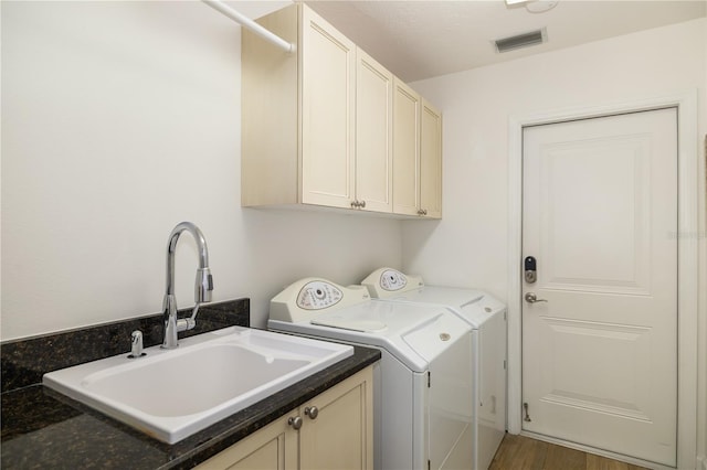 laundry area with visible vents, separate washer and dryer, wood finished floors, cabinet space, and a sink