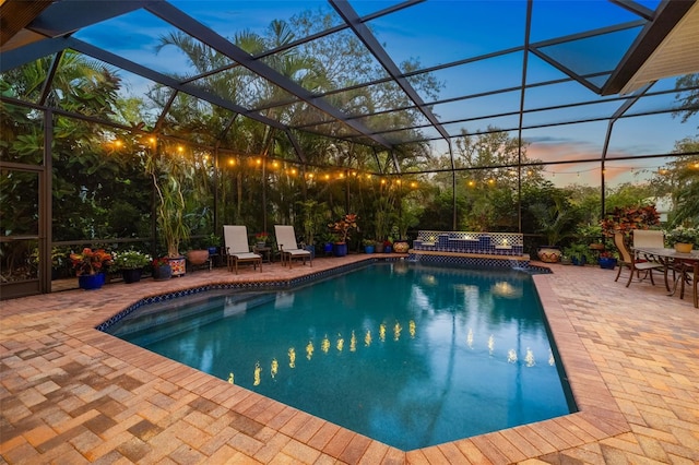 pool at dusk with a patio area, glass enclosure, and an outdoor pool